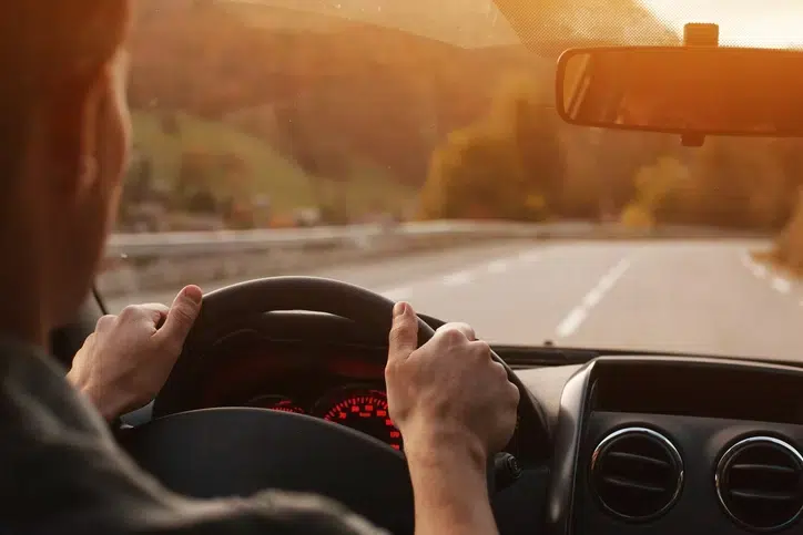 close up image of a man driving holding the steering with both hands. Picture shot from behind only showing the back part of his head