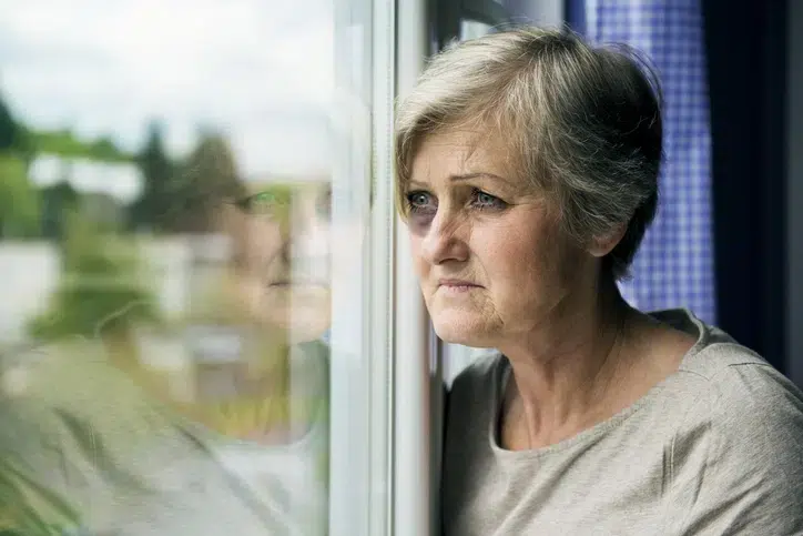 Physically abused sad old lady looking through the window with a black eye