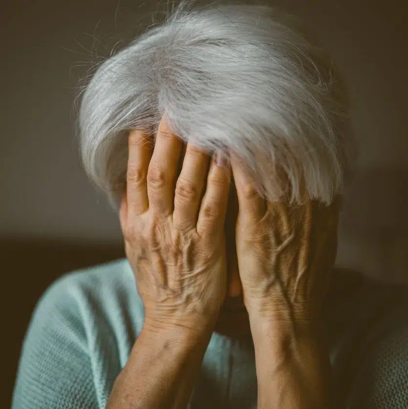 stressed elderly person with gray hair covering face with both hands